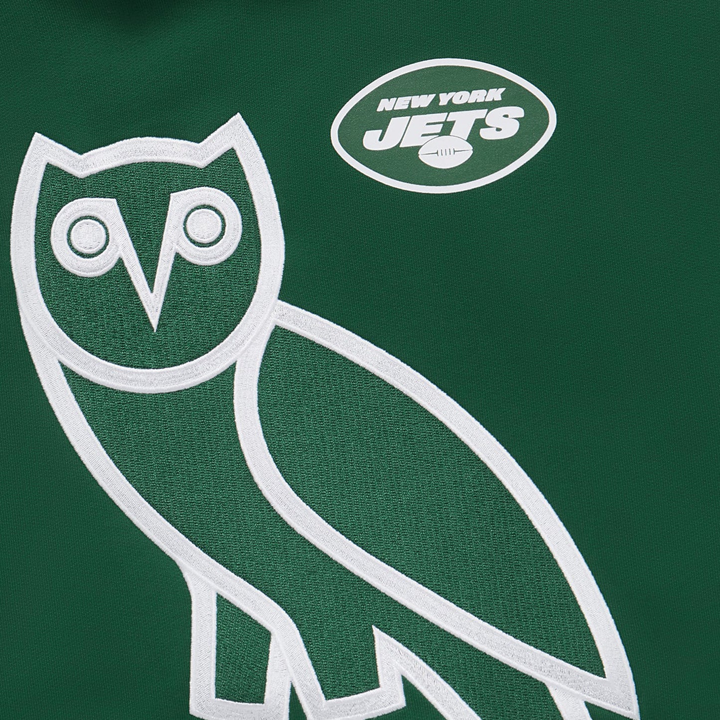 Close-up of the OVO owl logo and New York Jets emblem on a green hoodie.